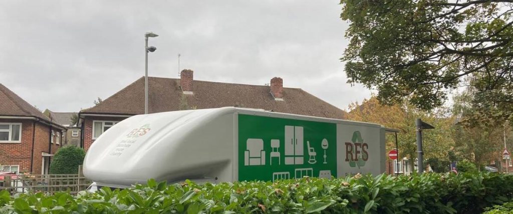 RFS white and green electric van with the top half exposed above a tall hedge
